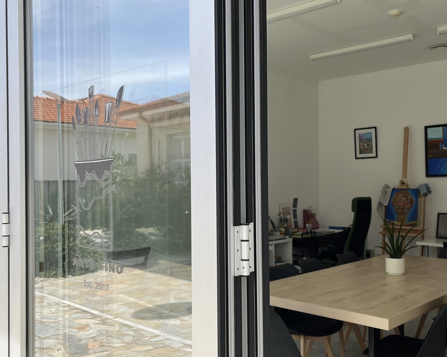 Inside Arte Fino studio — wooden table, plant and natural light through glass doors